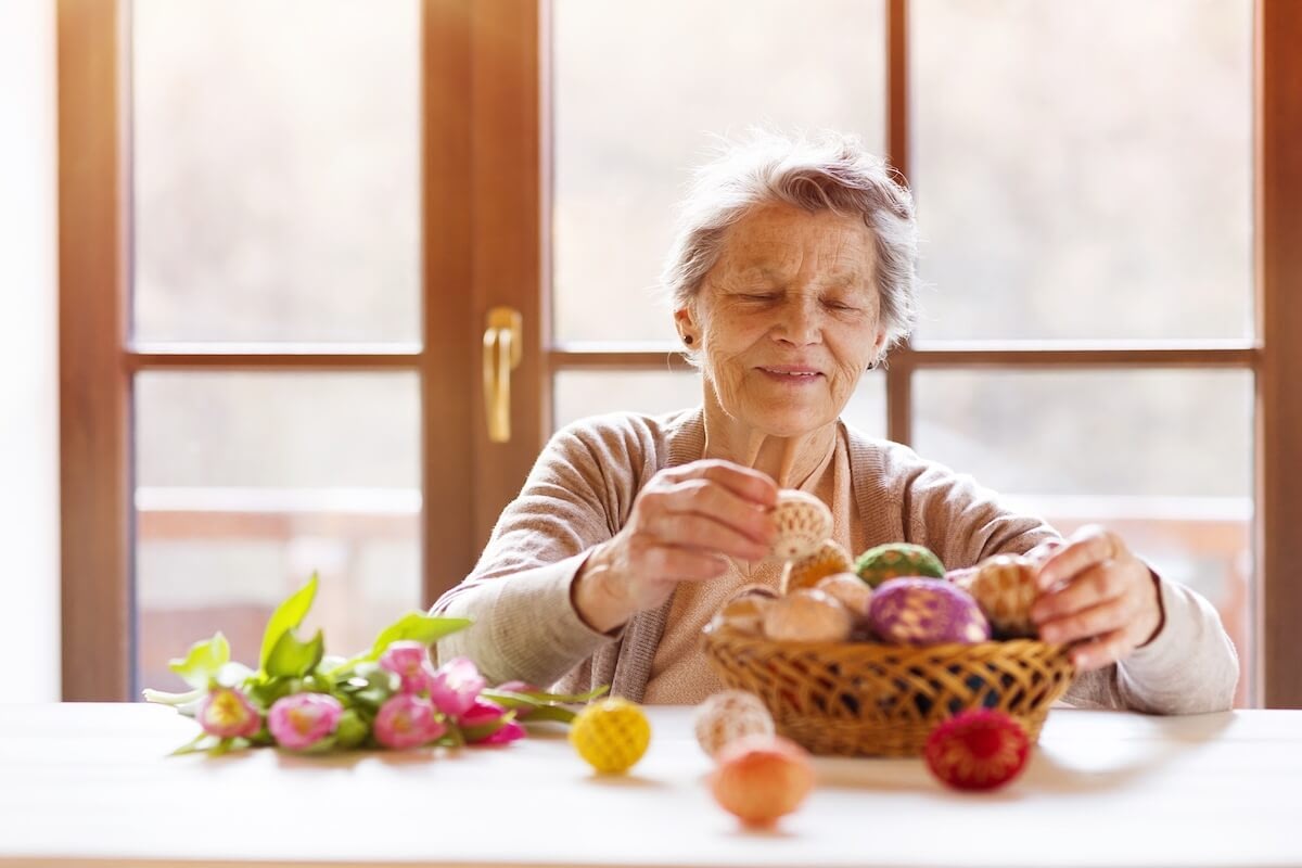 Senior woman decorating colorful Easter eggs indoors