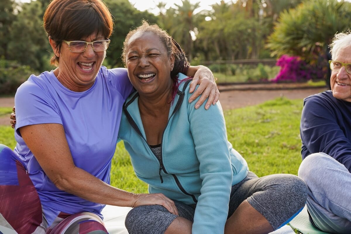 Three seniors laughing during outdoor yoga session