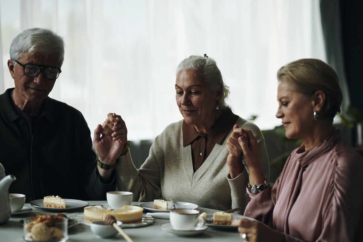 Three seniors holding hands before dessert and tea