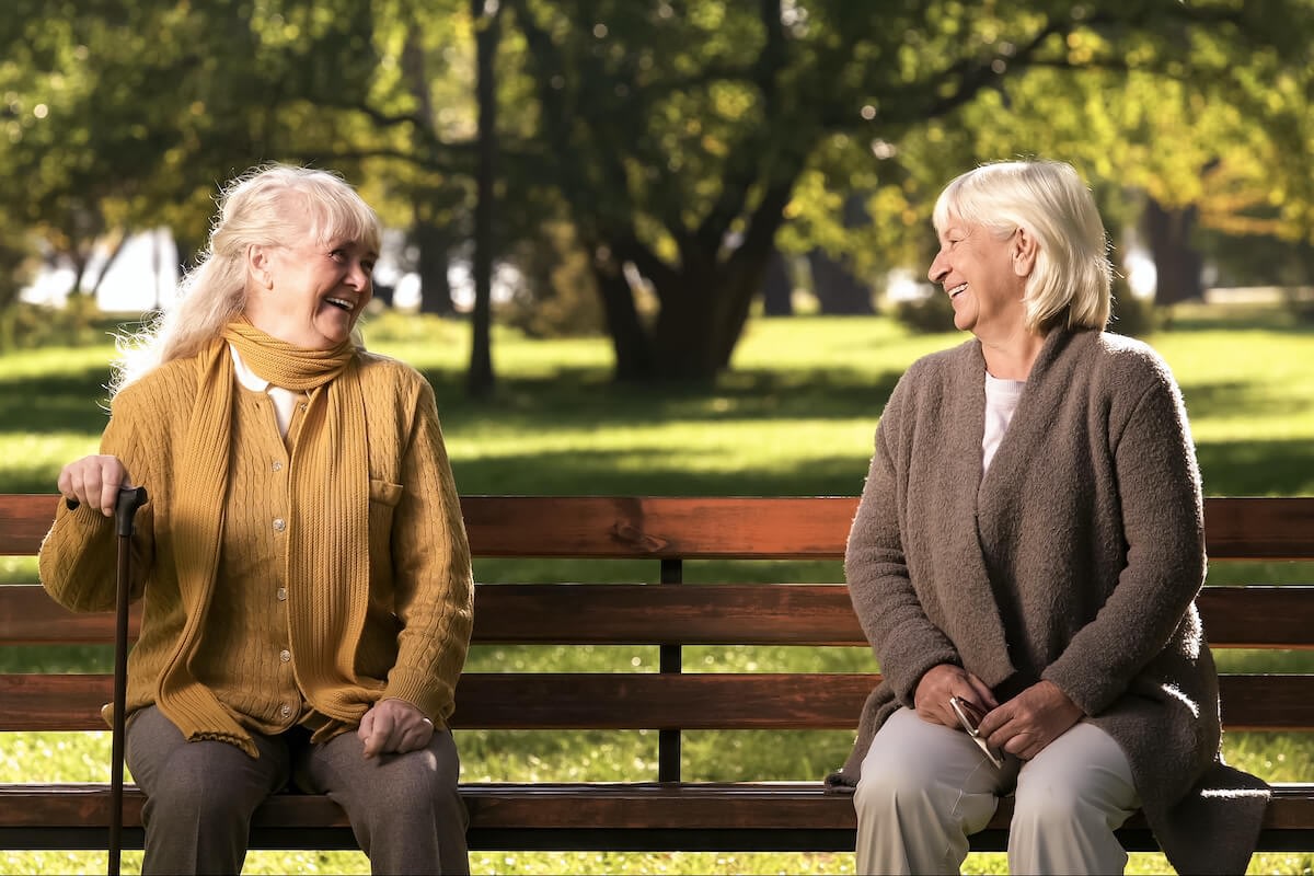 Two elderly women smiling on park bench
