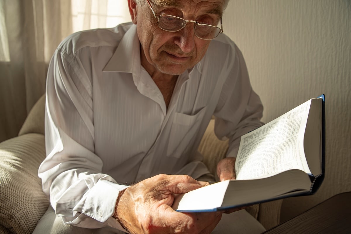 Elderly man reading book by window light