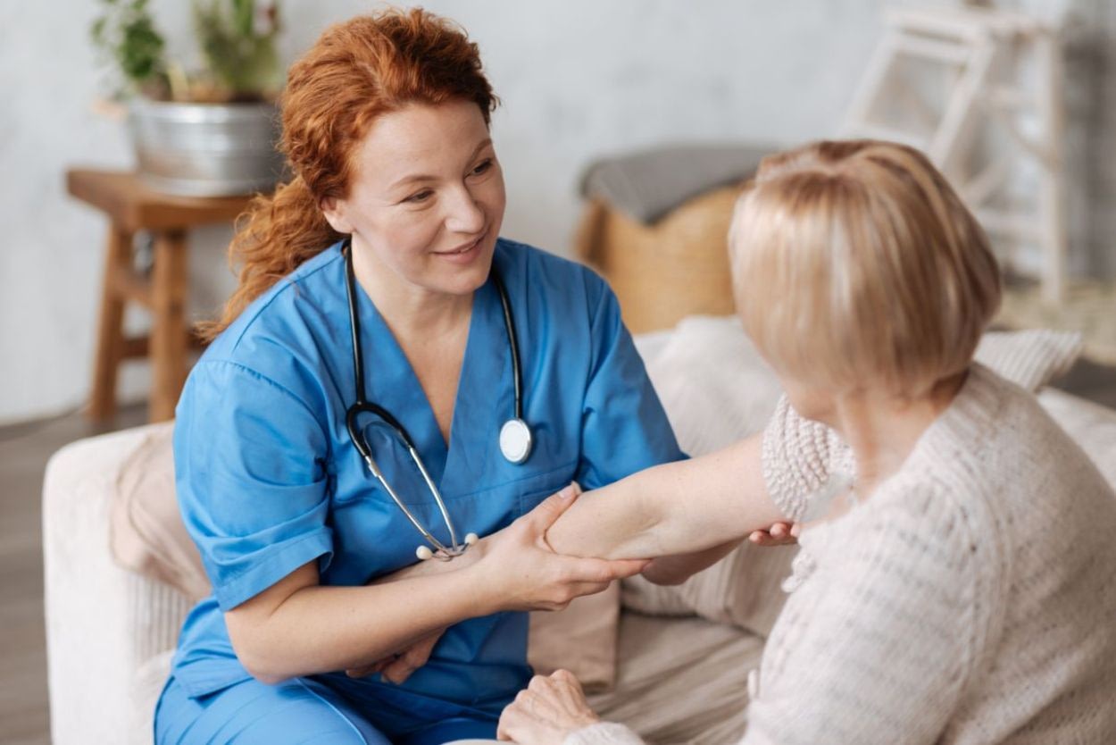 Nurse examining elderly woman's arm at home