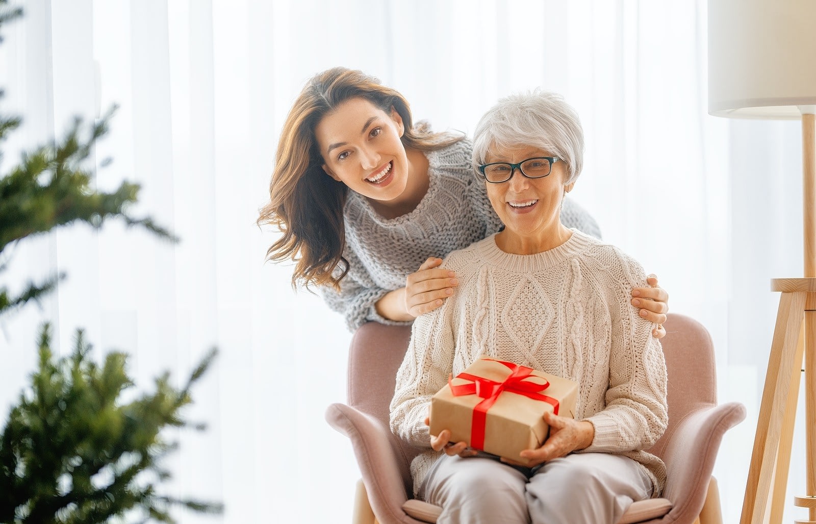 Young woman surprising senior with wrapped gift