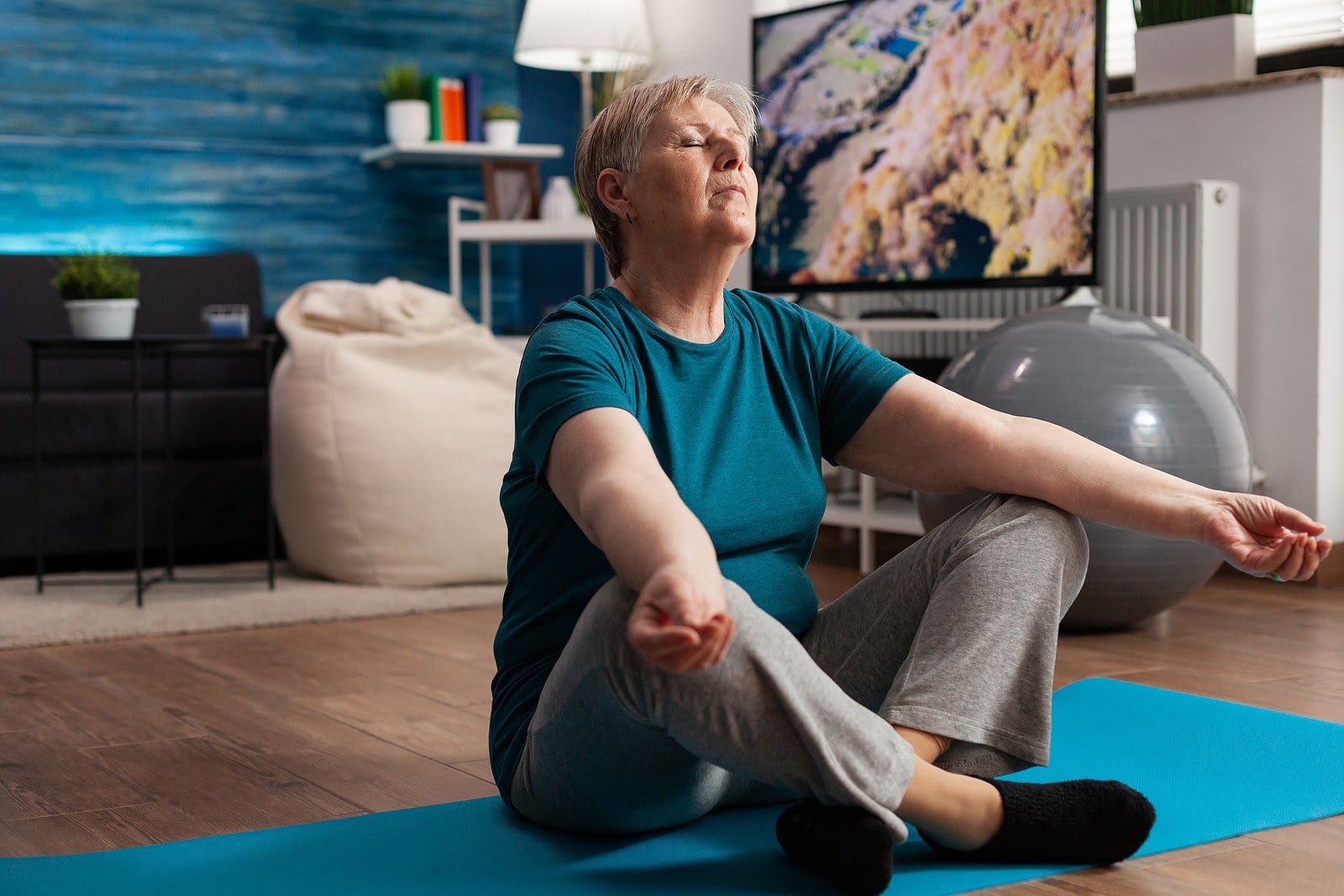 Older woman meditating on yoga mat at home