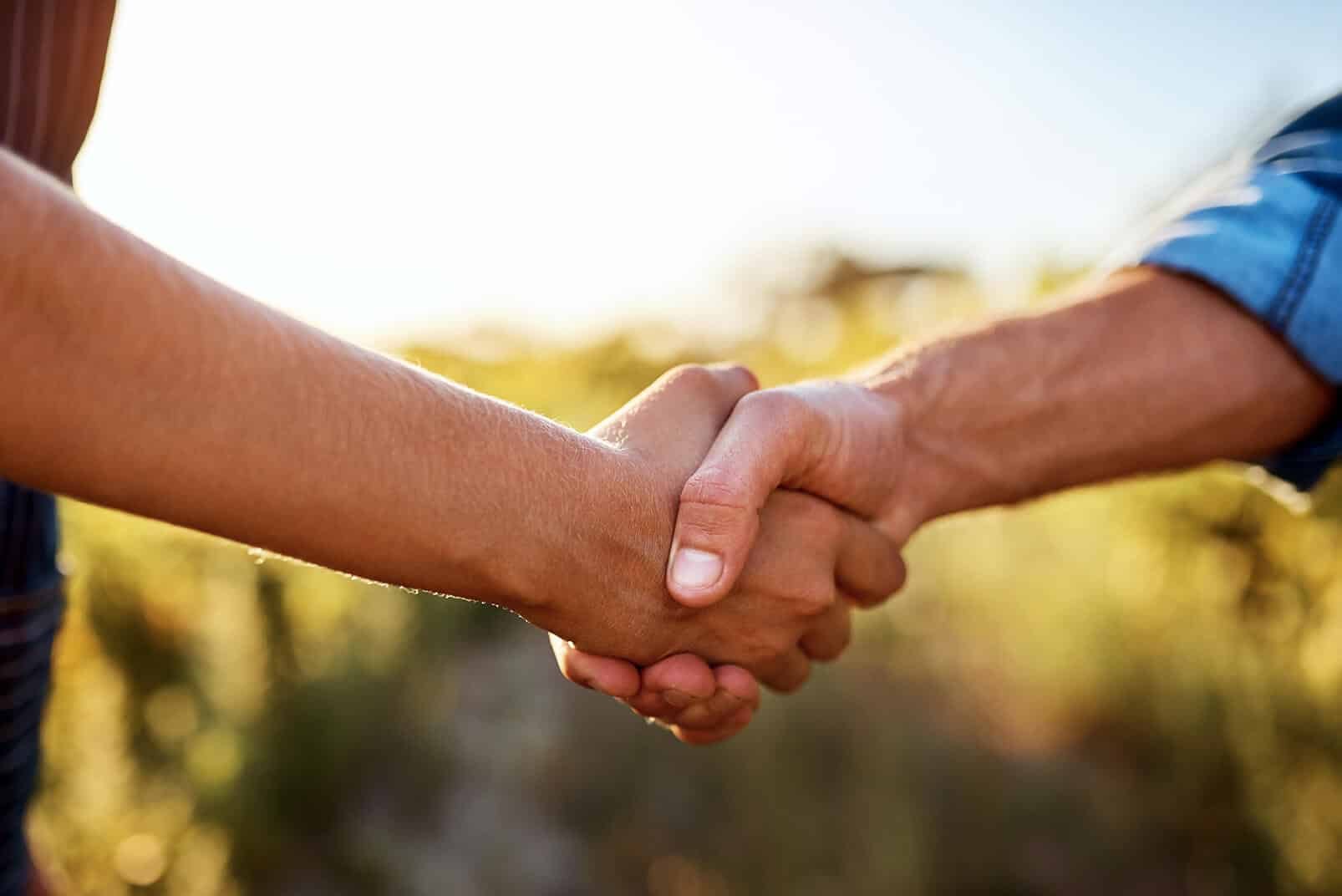 Two people shaking hands outdoors at sunset