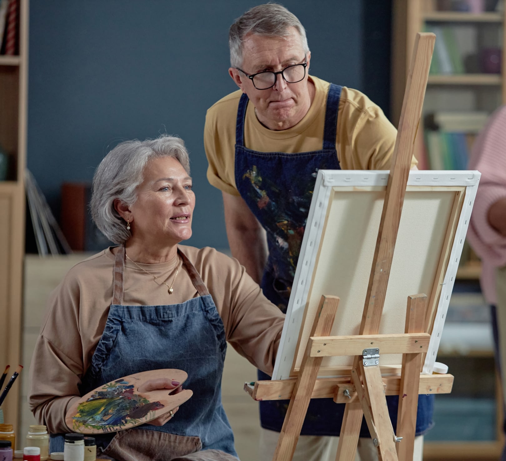 Senior woman painting at easel with instructor