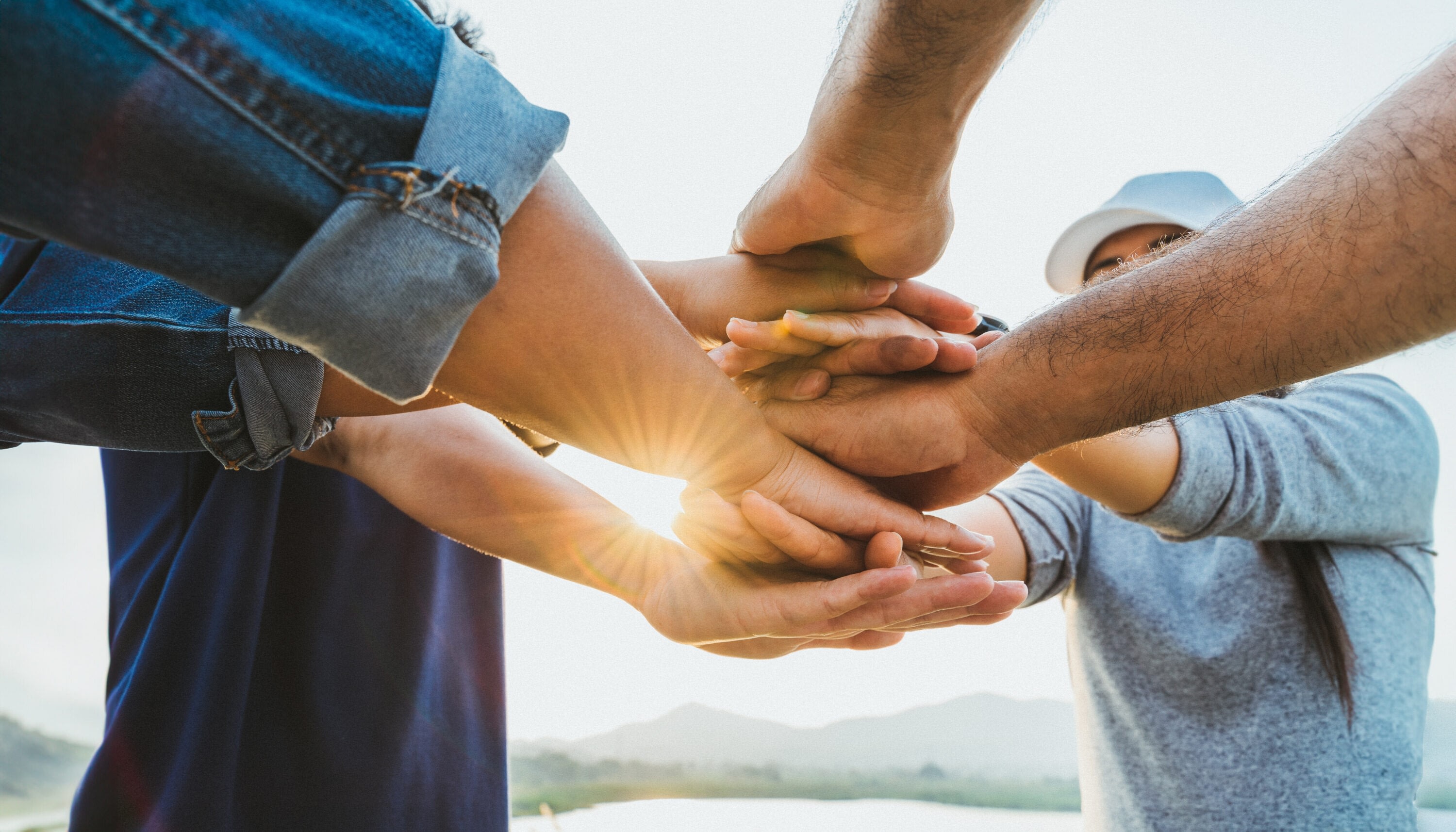 Group of people stacking hands outdoors in sunlight
