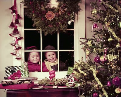 Two children peeking through window at Christmas tree
