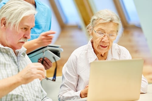 Elderly couple using laptop with caregiver assistance