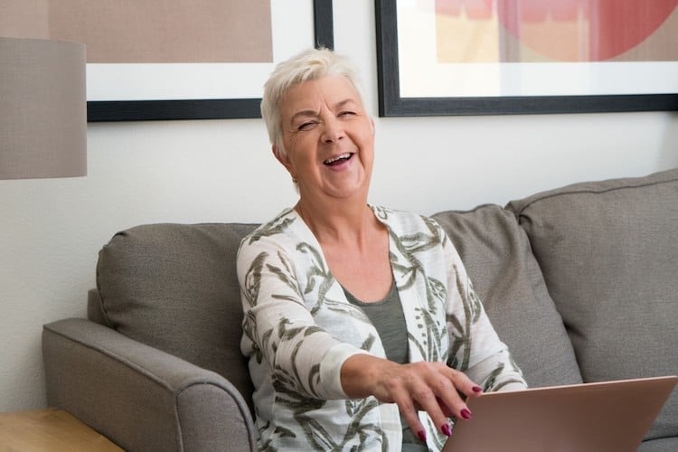 Smiling older woman using laptop on couch