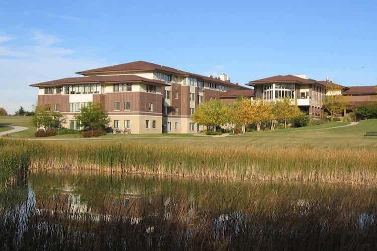 Modern campus building beside pond and grassy lawn