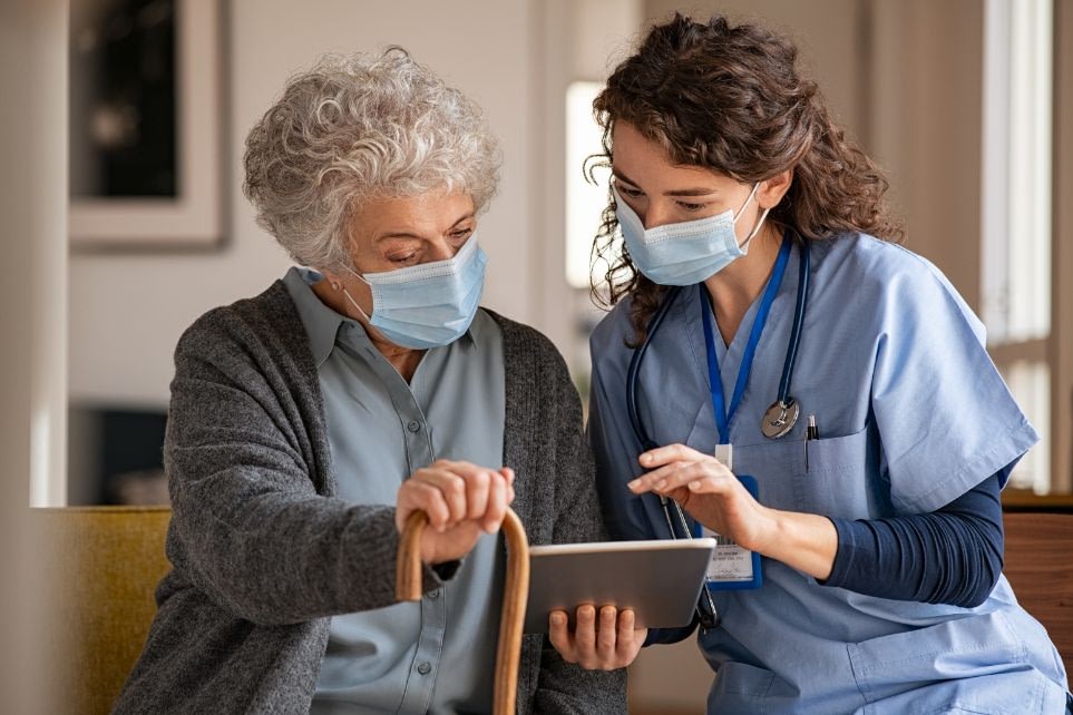 Nurse assisting elderly woman with tablet and cane