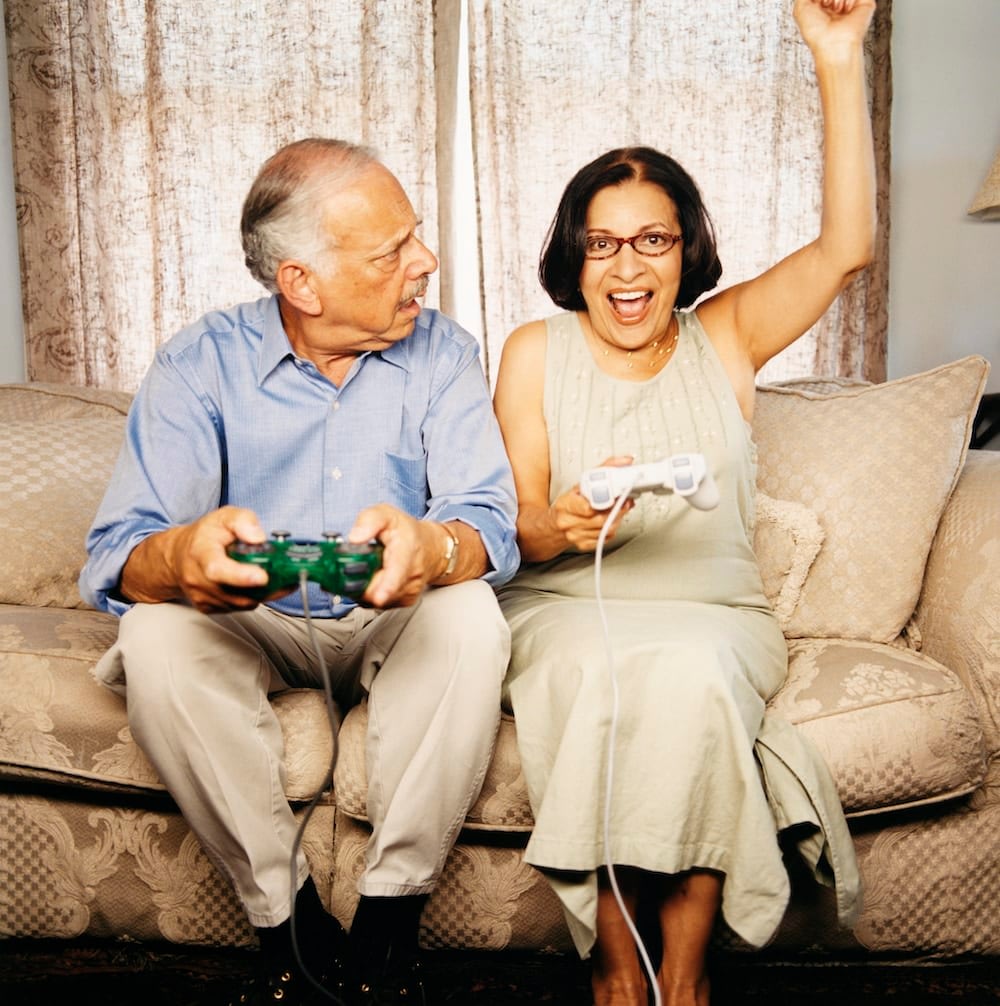 Older couple sitting on couch while holding game controllers, woman pumping fist in air and man looking disgruntled