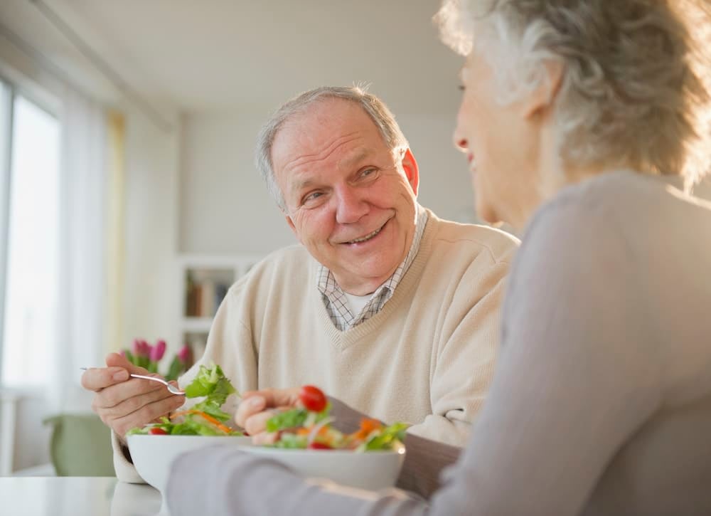 Older man and older woman smiling while eating salad