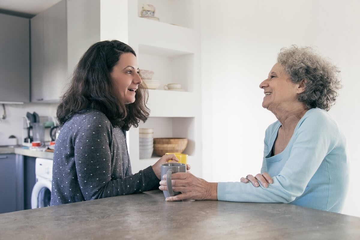 Two women smiling with coffee in kitchen