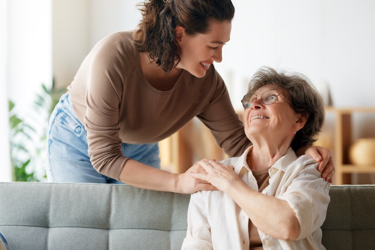 Daughter embracing elderly mother on living room couch
