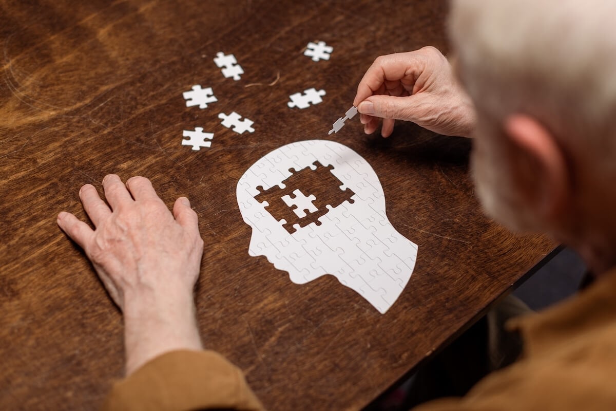 Senior man placing puzzle piece in head silhouette