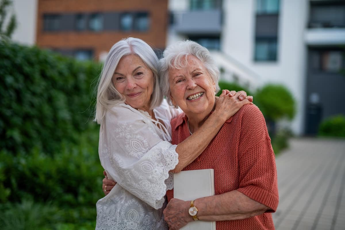 Two elderly women hugging and smiling outdoors
