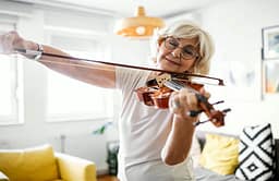 Older woman playing violin in bright living room