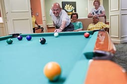 Elderly man playing pool with friends indoors