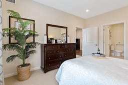 Staged bedroom with dresser, mirror, and open bathroom