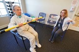 Senior woman exercising with therapist using bar