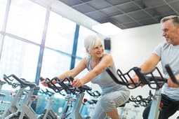 Senior couple exercising on stationary bikes at gym