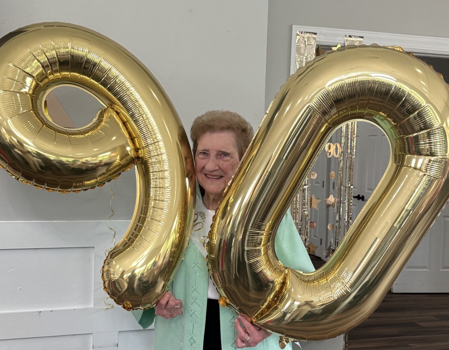 Smiling woman celebrates with large gold 90 balloons.