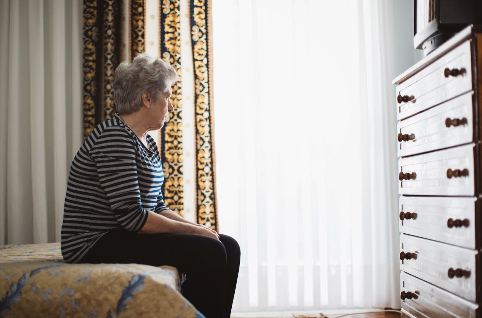 Older woman with blank expression sitting at end of bed