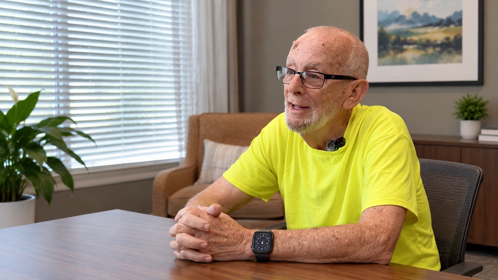 Older man in yellow shirt speaking at table