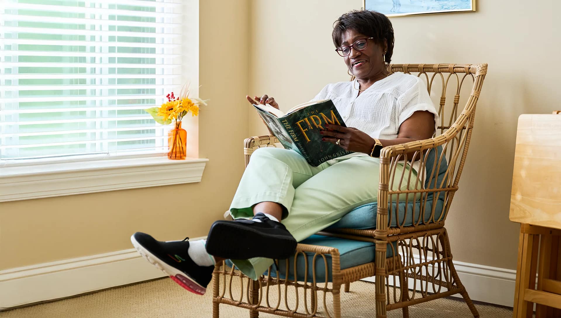 Woman reading book in wicker chair by window