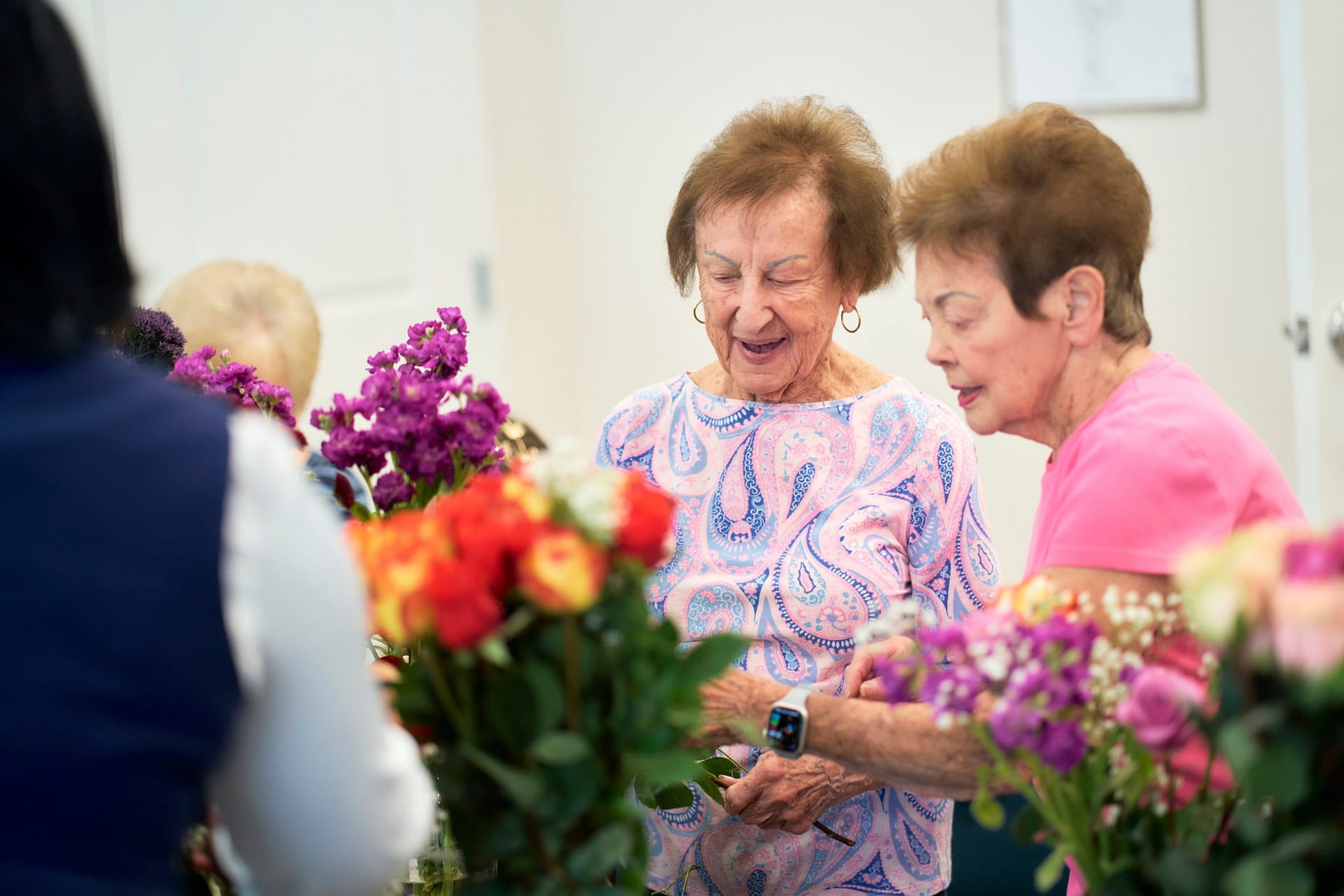Elderly women arranging colorful flowers indoors
