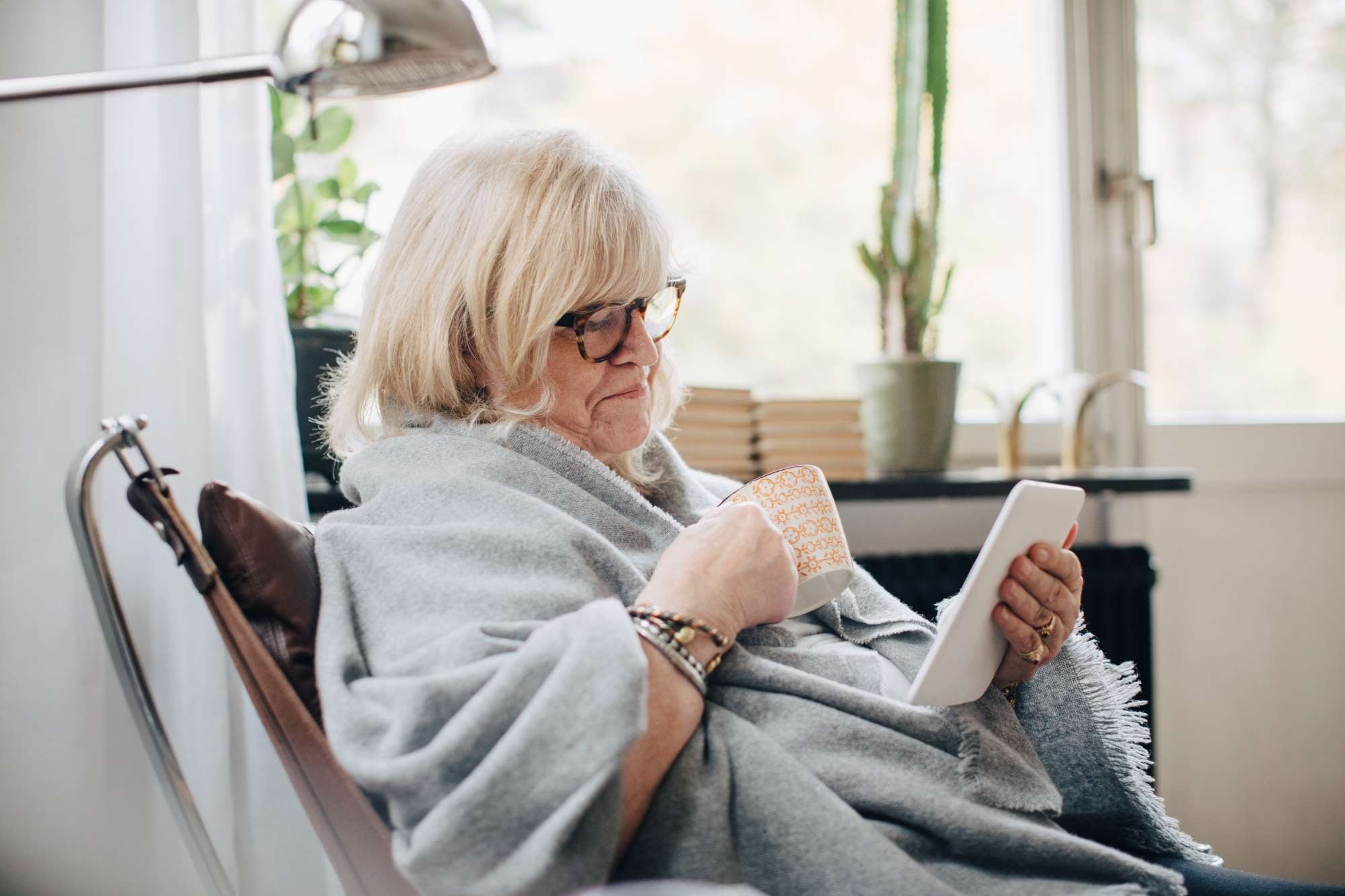 Older woman wrapped in a blanket looking at a tablet while sitting in a chair