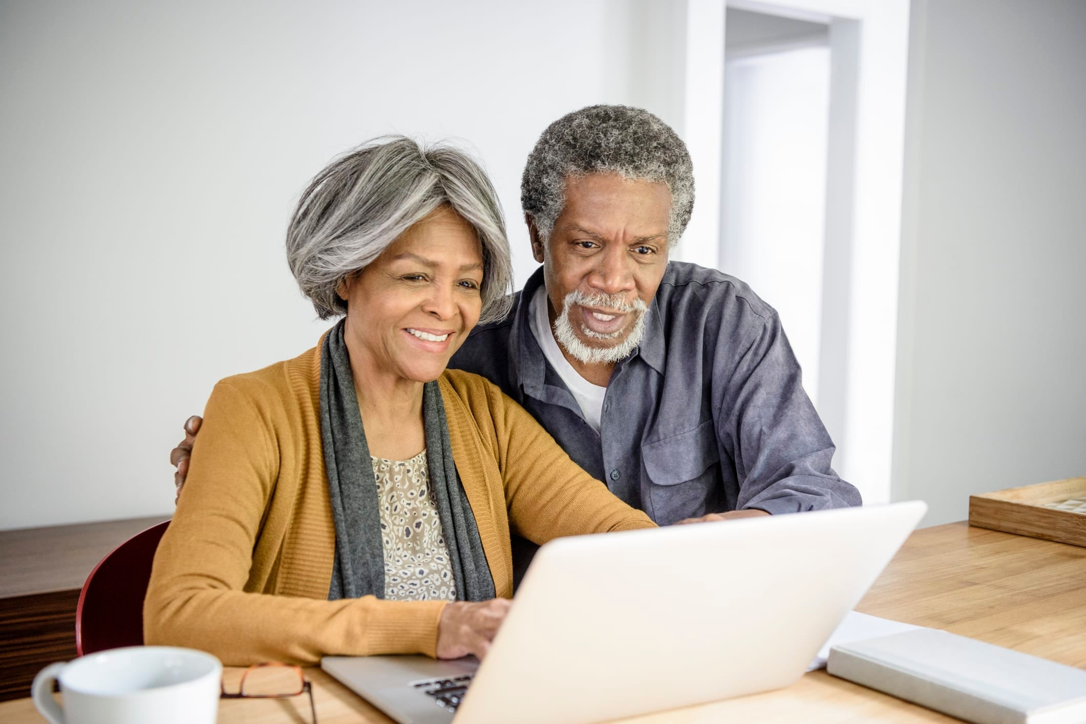 Senior couple looking at laptop together at home. The woman is typing and the man is watching with his arm around her at Brightwater Senior Living of Tuxedo in Winnipeg, Manitoba