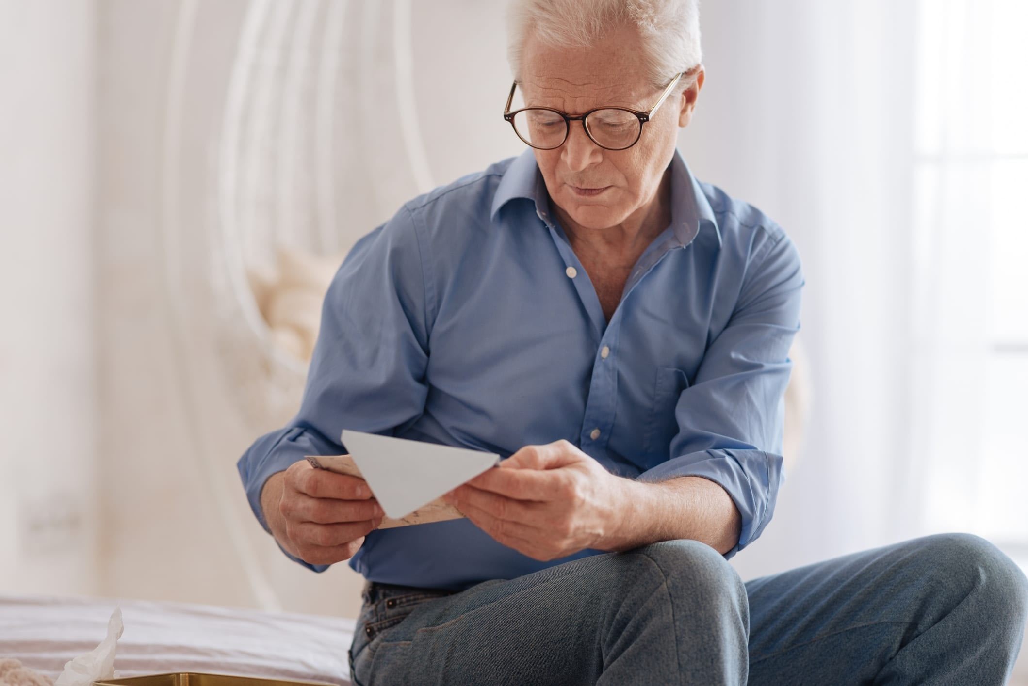 Elderly man with glasses sitting down and looking at an envelope.