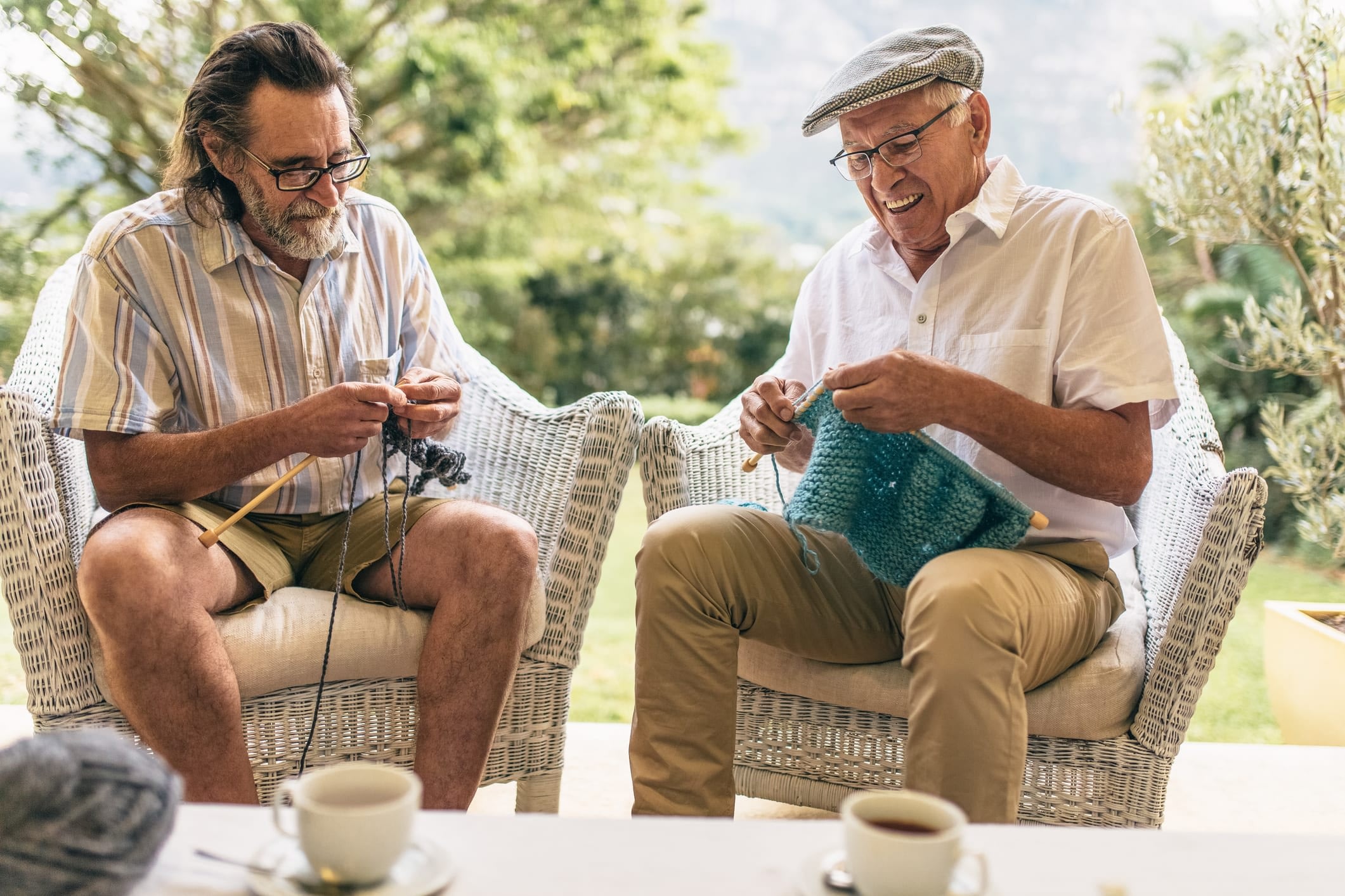 Two senior men sitting in armchairs and knitting.