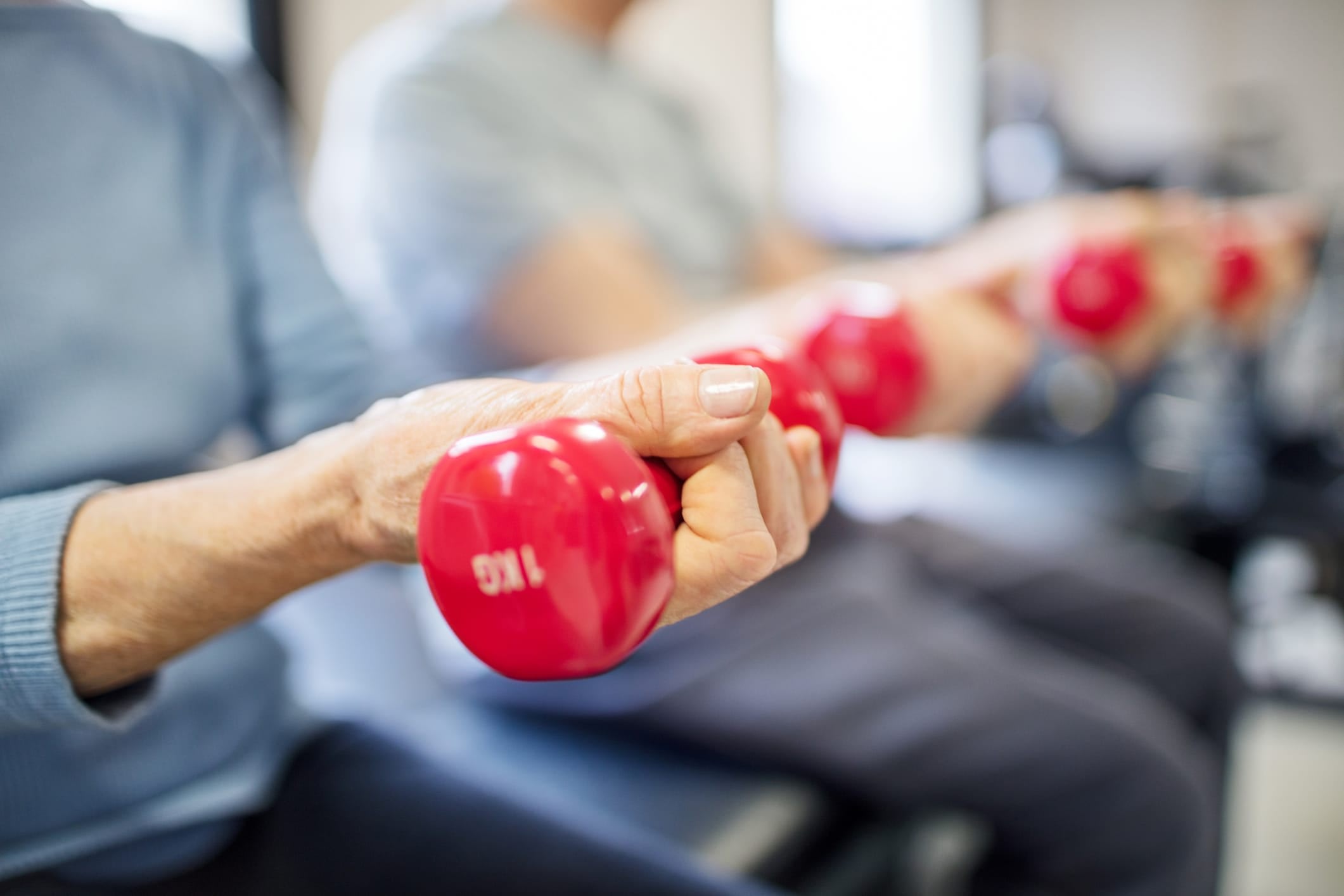 Close up of two women seated lifting up a pair of red dumbbell weights