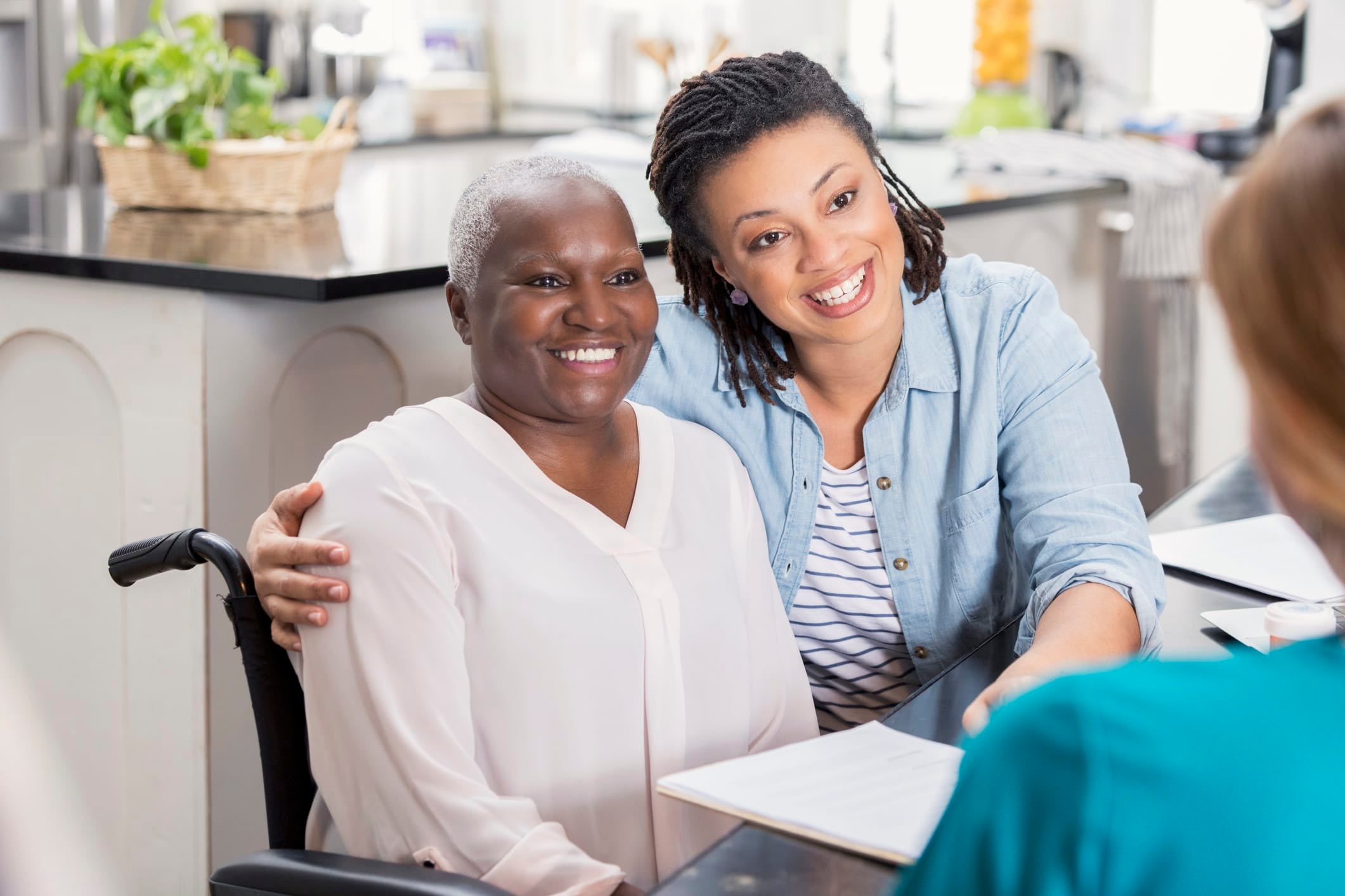 Senior woman in a wheelchair and younger woman smiling and looking toward person in foreground.