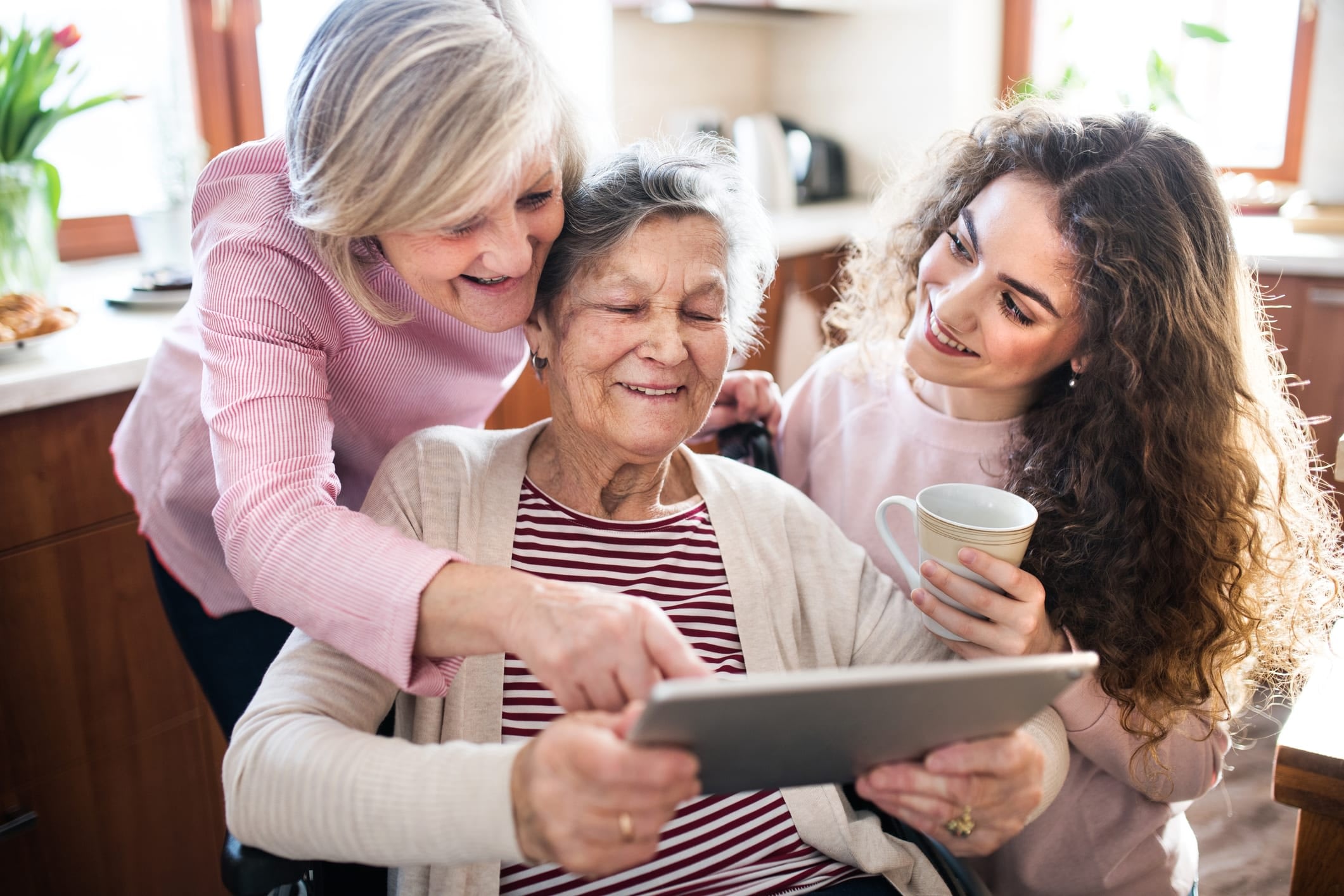 A middle-aged woman, elderly woman, and young woman look at a tablet together.