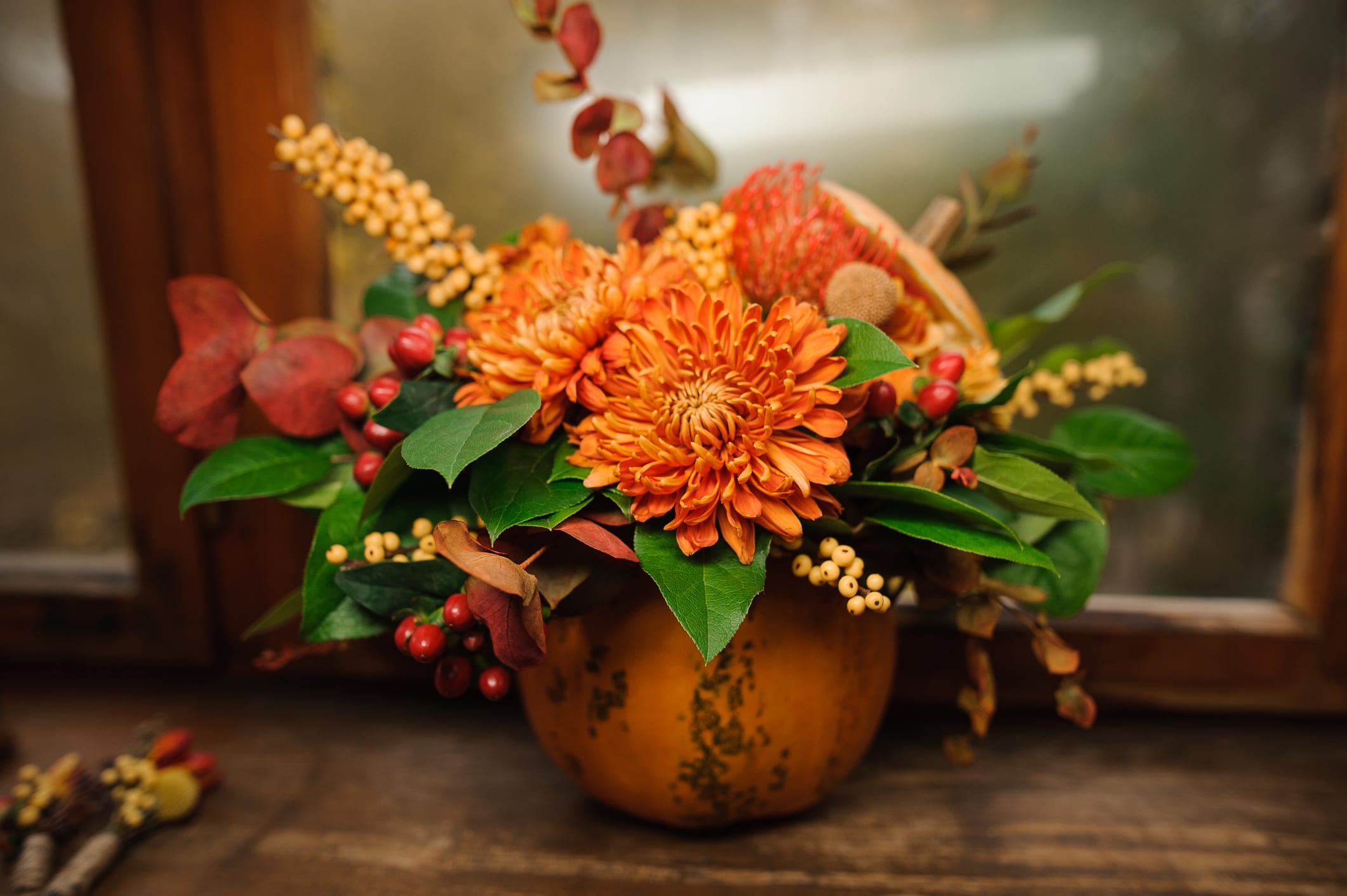 A small pumpkin has been hollowed out from the top to make a natural vase and filled with flowers, berries, and greenery.