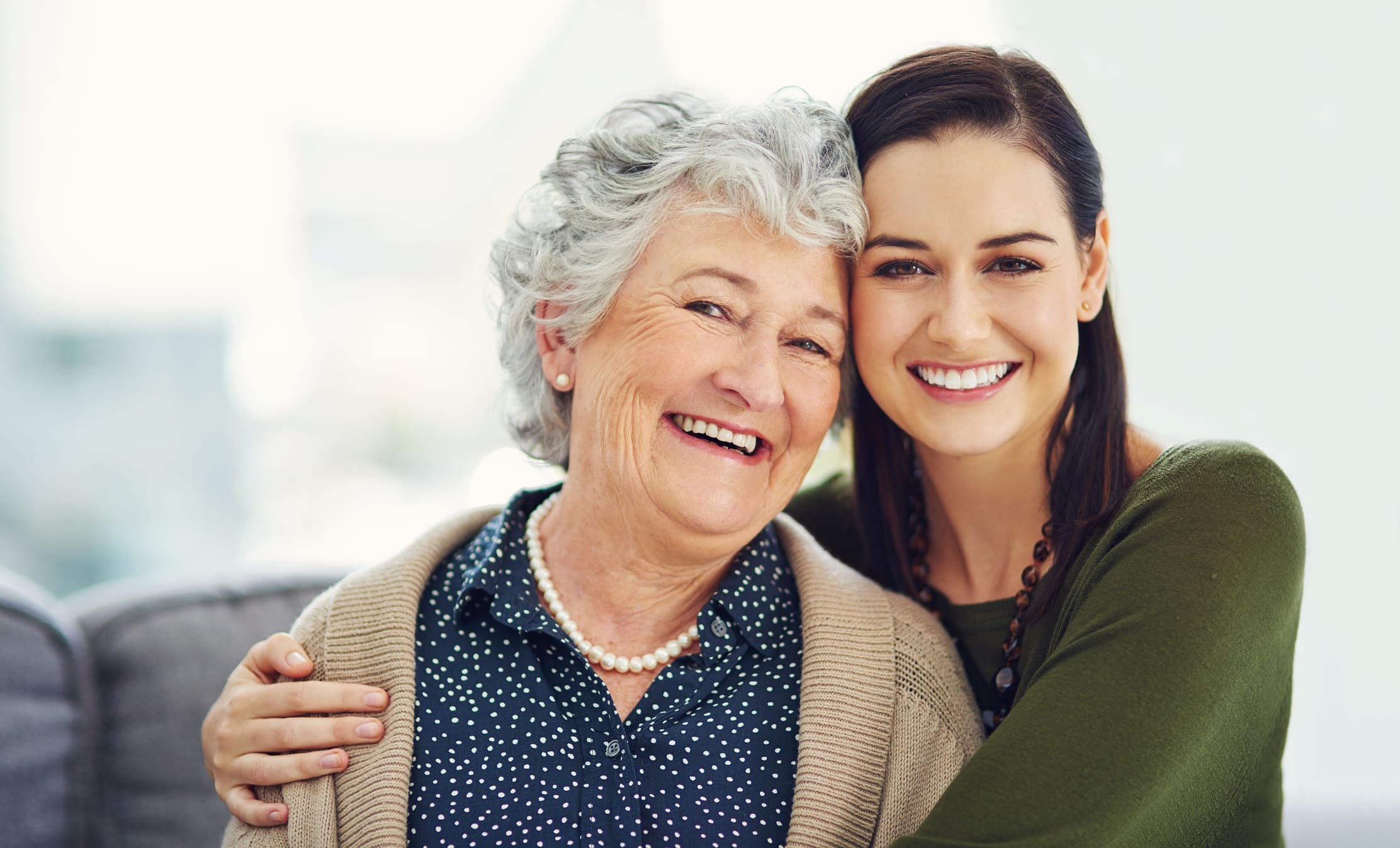 Senior mother and adult daughter hugging and smiling.