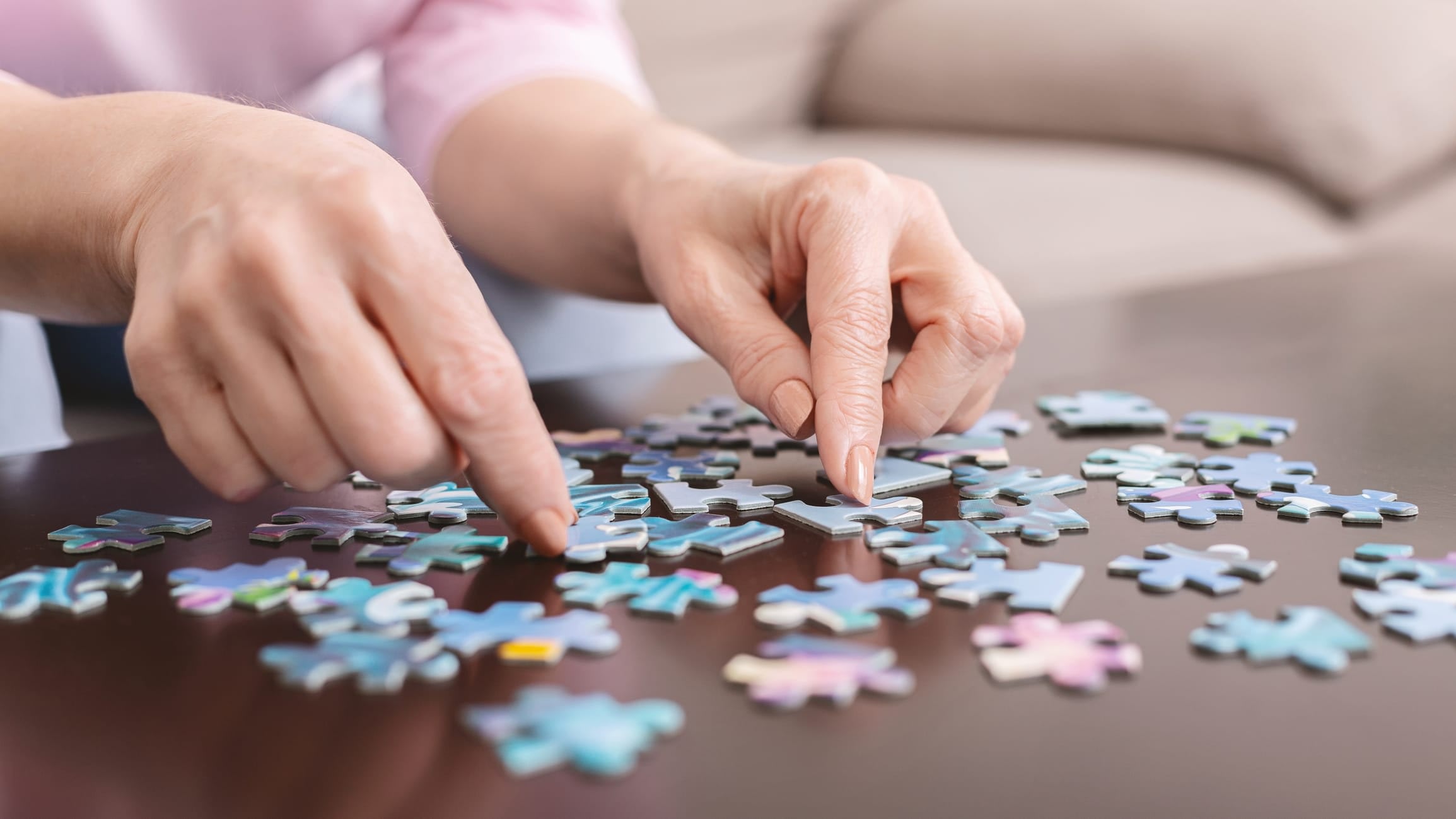 Closeup of a senior woman’s hands solving a jigsaw puzzle on a table.