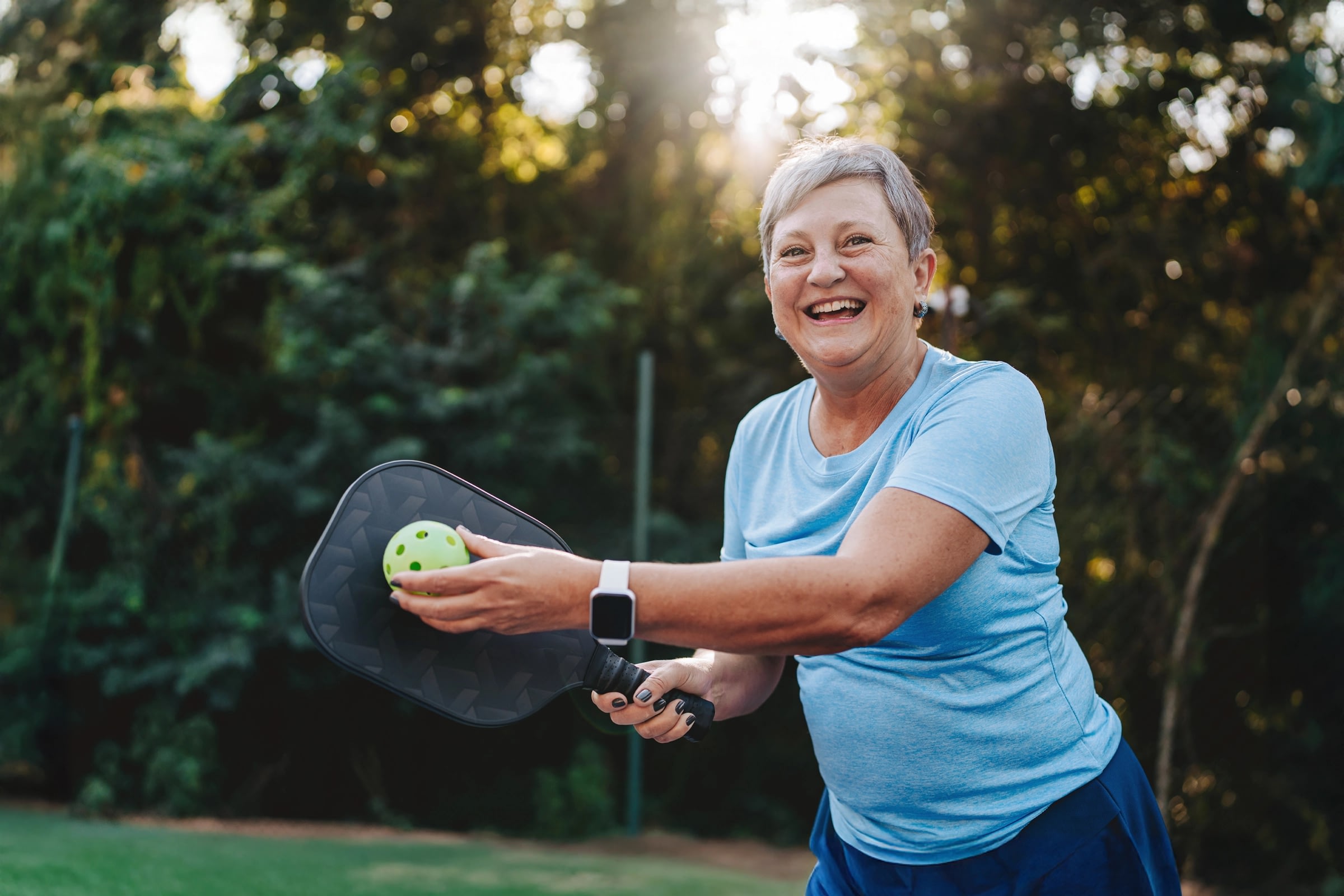 Smiling older woman playing pickleball outdoors