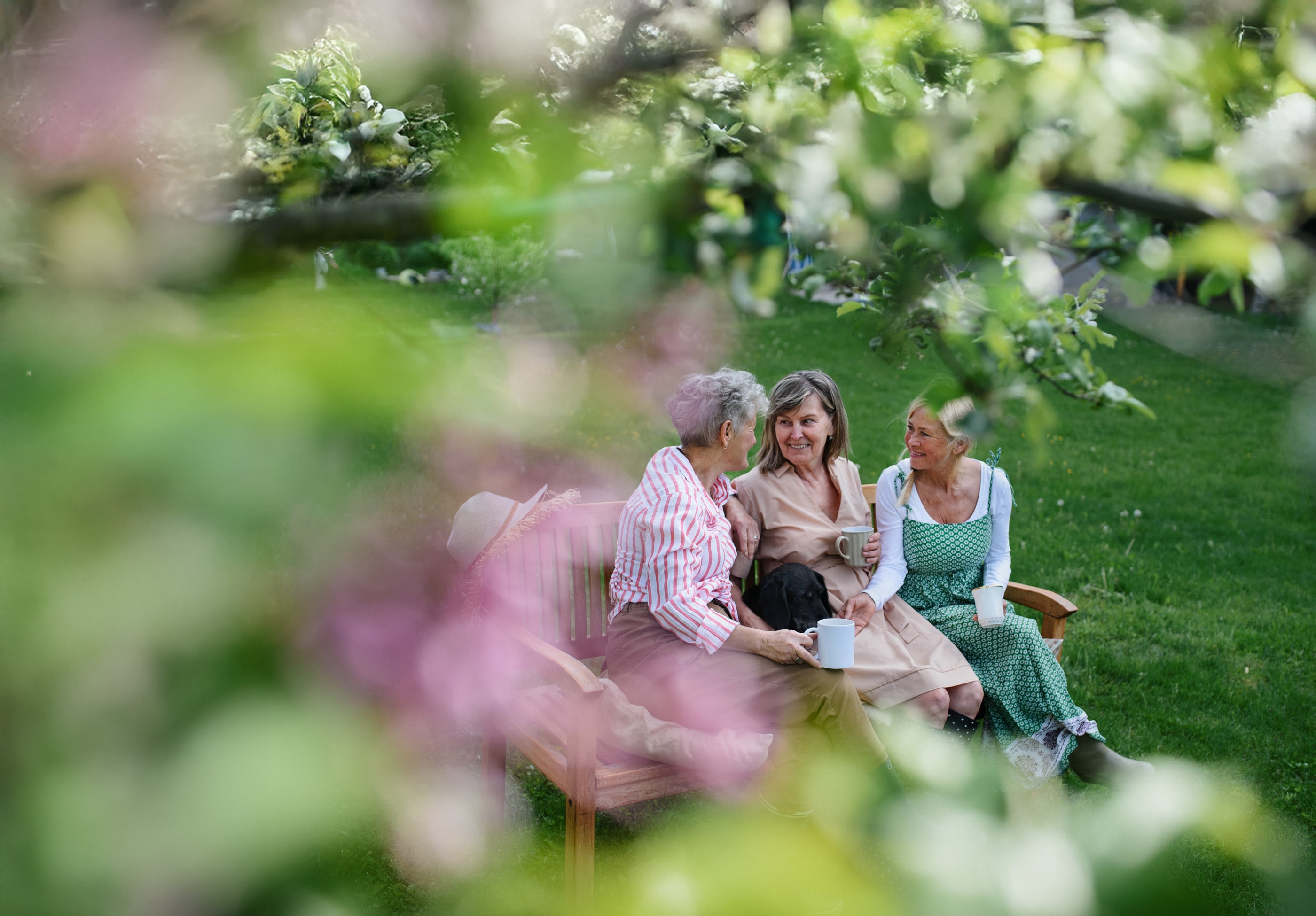 Three women chatting on garden bench with mugs