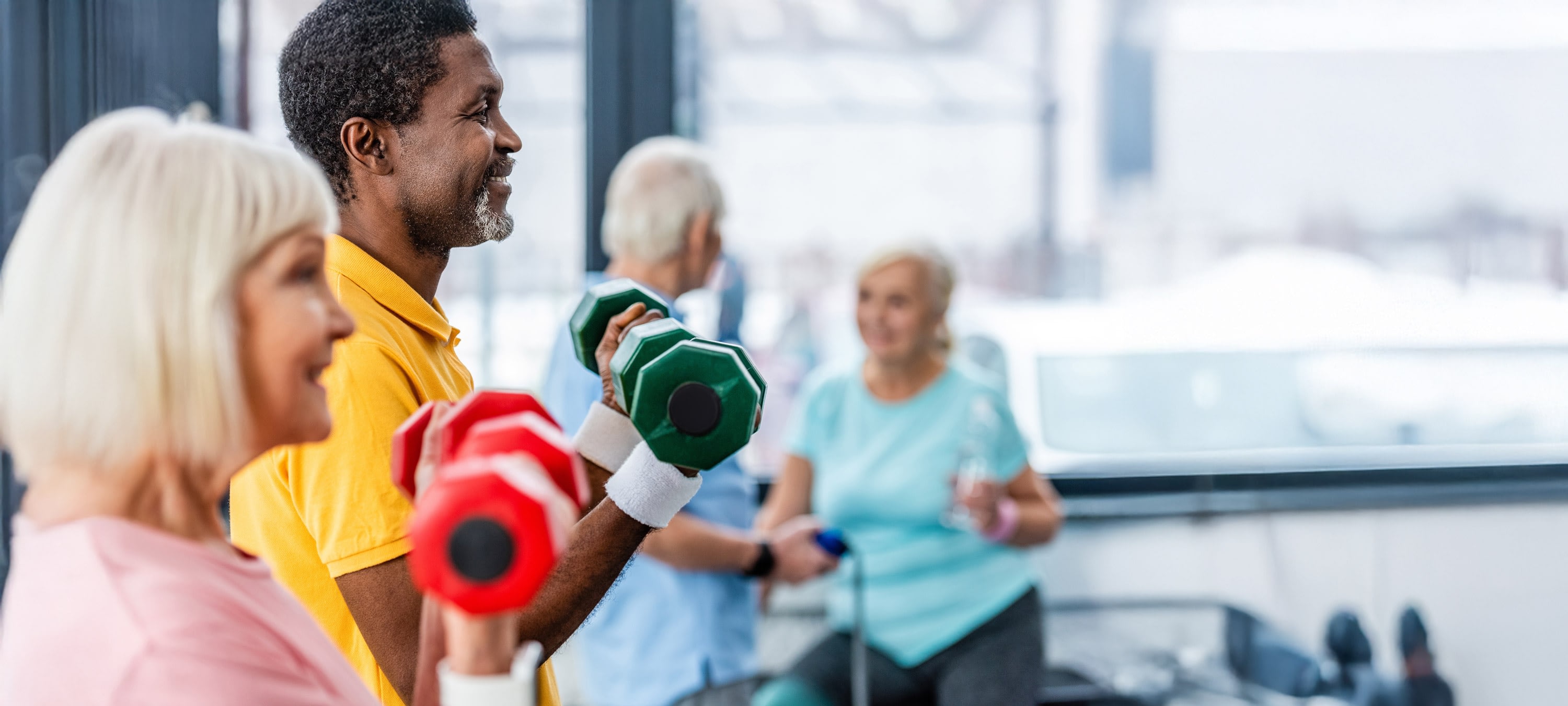 Older adults lifting dumbbells in bright gym