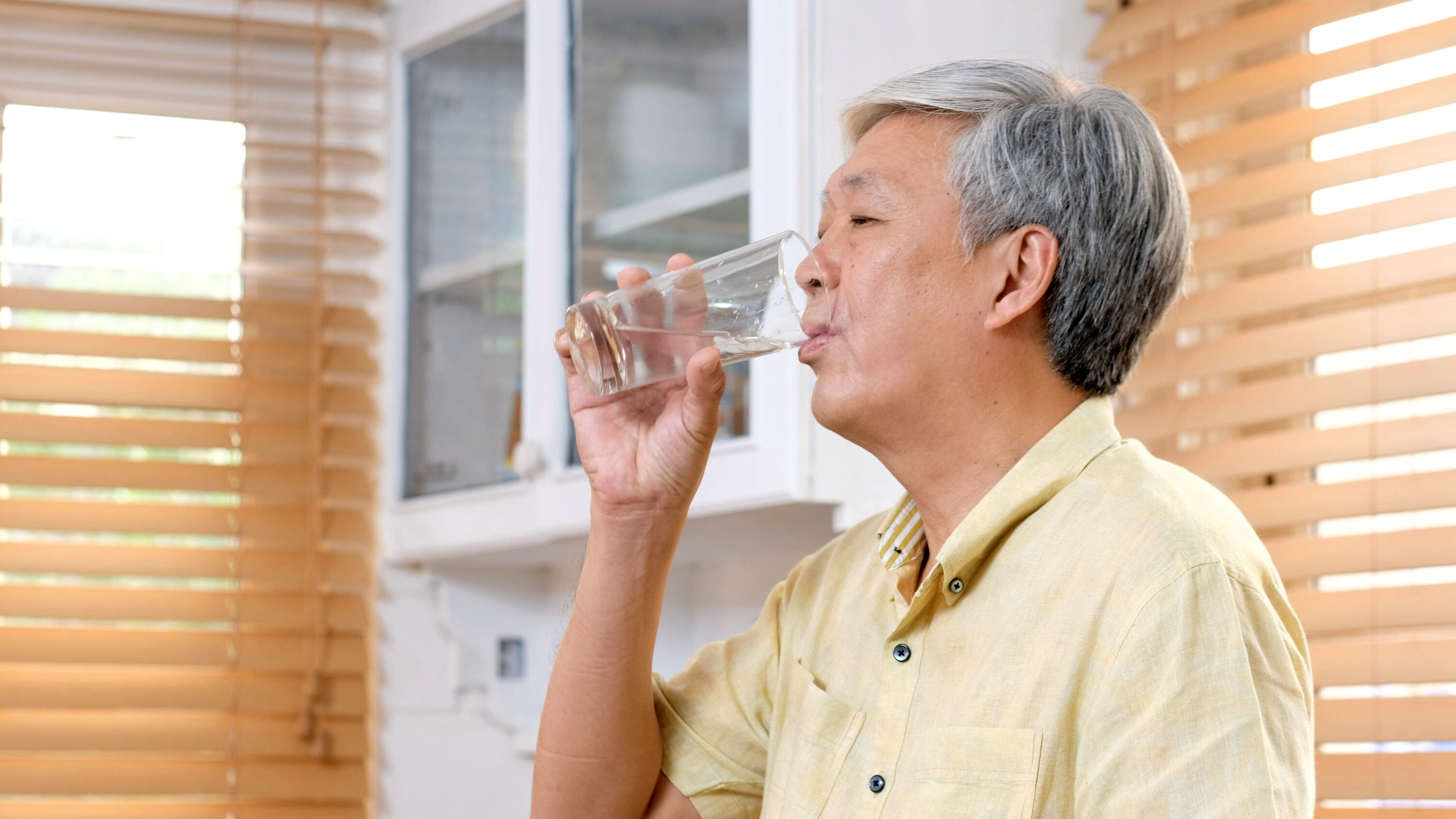 Senior man drinking a glass of water in a kitchen.