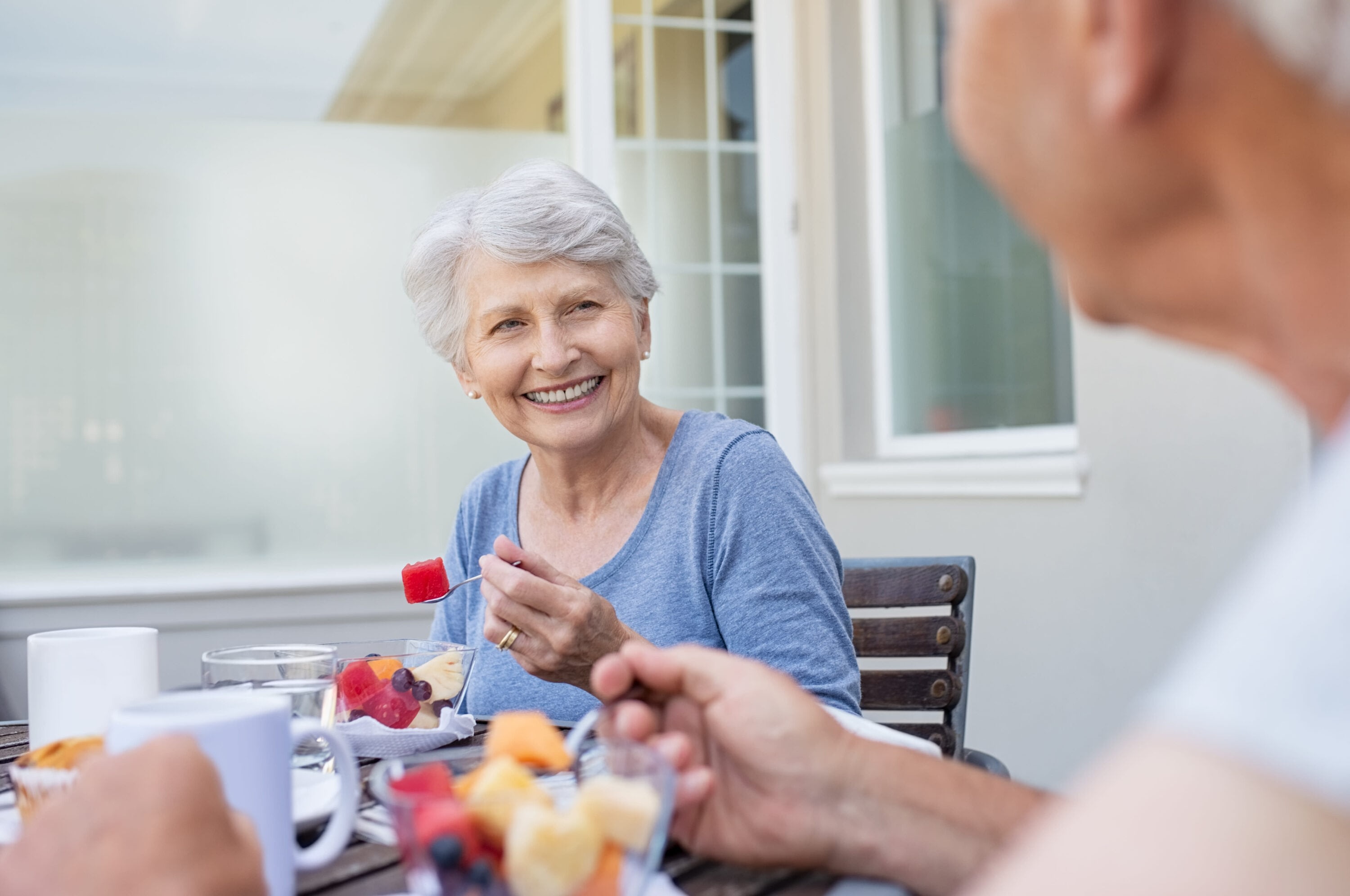 Senior woman smiling looking at a senior man while eating fruit.