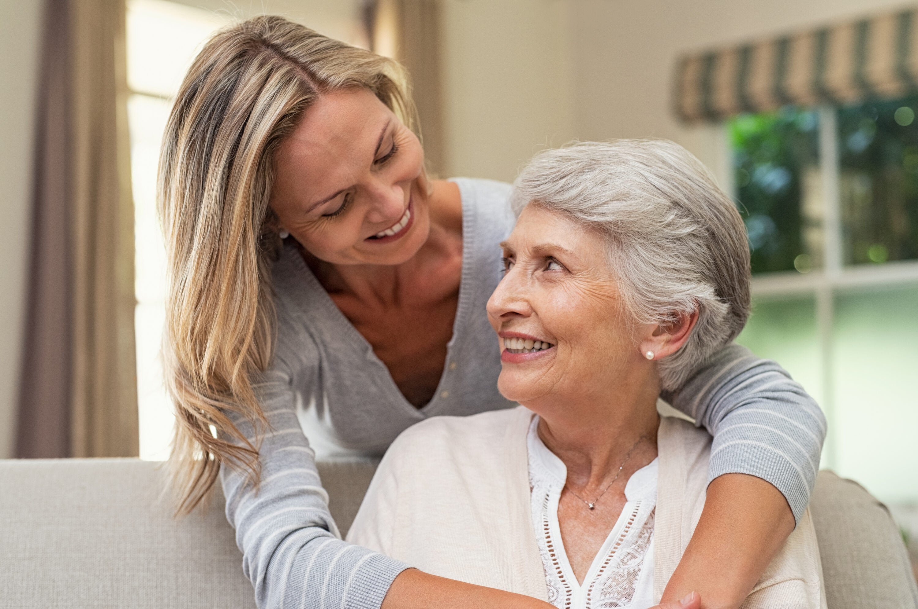 Smiling older woman and daughter laughing together in sunlit room