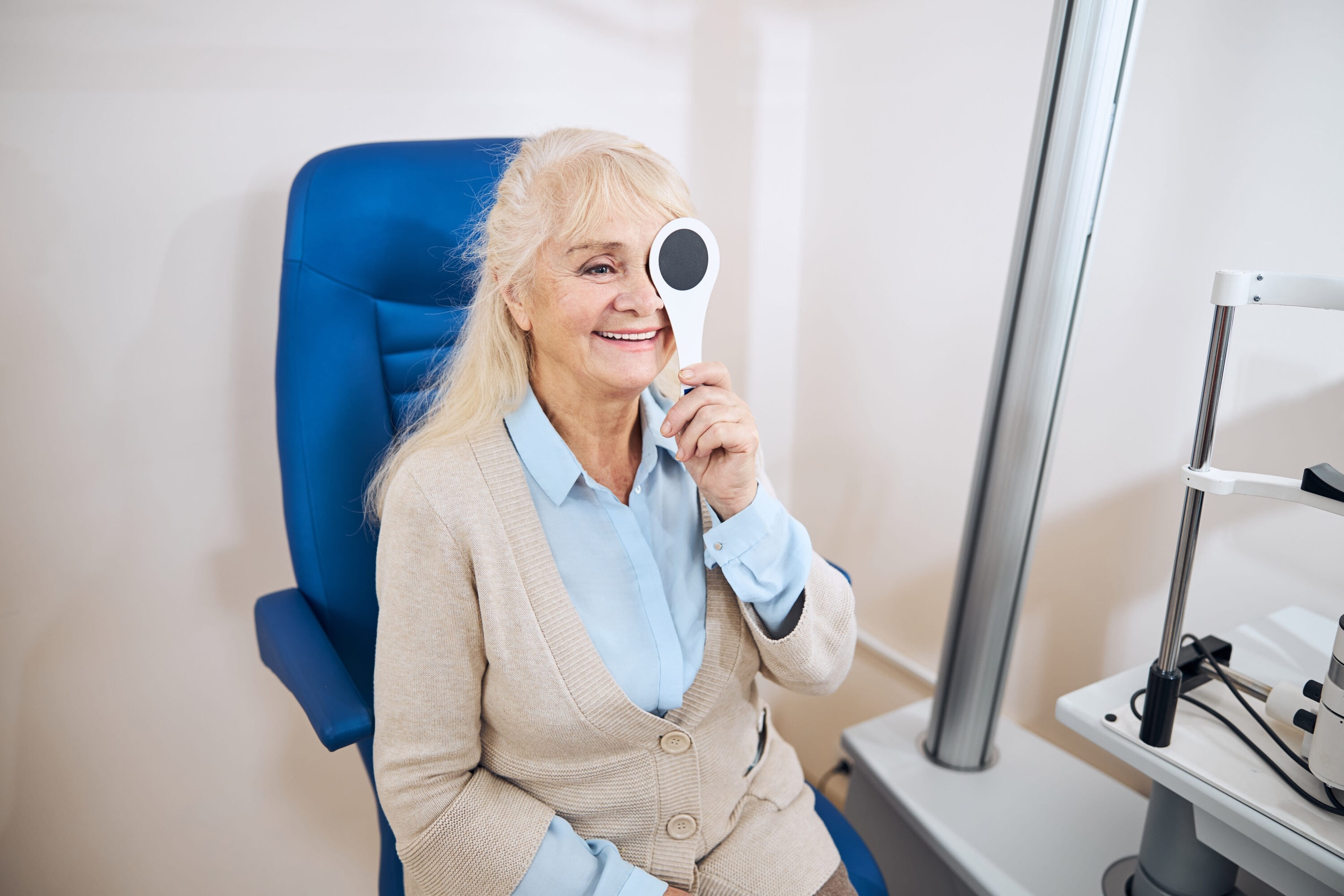 A smiling older woman covers one eye during a vision test.