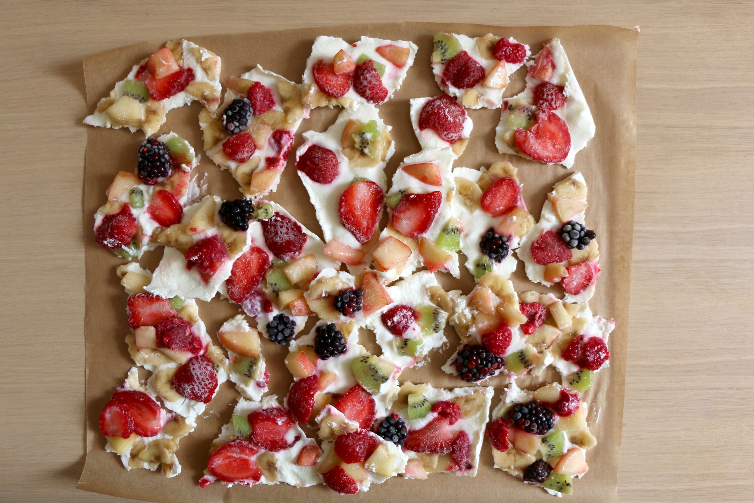 Overhead photo of pieces of frozen yogurt bark with various fruits on it, including strawberries, bananas, nectarines, kiwis, raspberries, and blackberries.